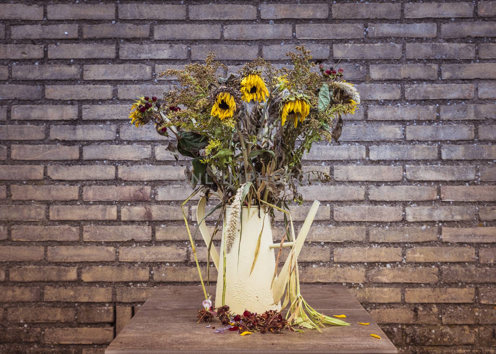 Looking slightly down at a vase of dying flower arrangement, large once bright now dying sun flowers in a vase on a very large marble dining table