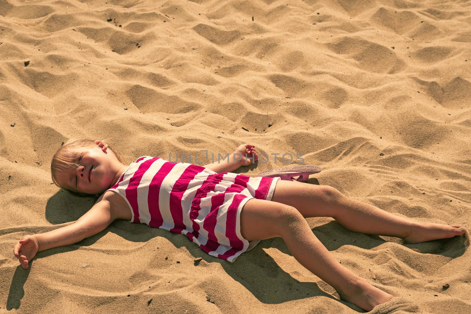 Baby girl lying on sand. Adorable kid sunbathing at summertime. Young child resting and relaxing with her eyes closed. Caucasian preschooler lying down portrait. Tranquil scene of dreaming girl child.