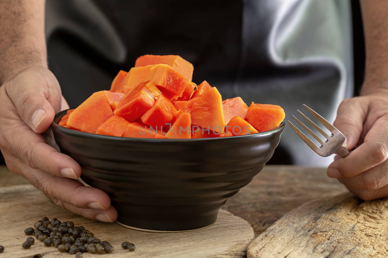 Ripe papaya fruit cut into pieces in a black bowl on wooden background.