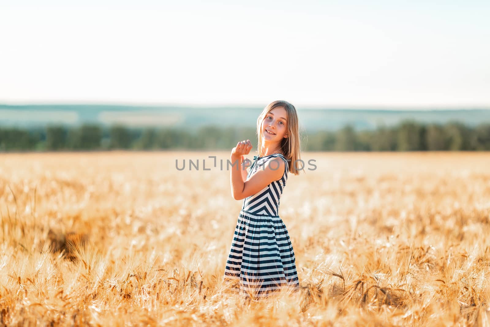 Happy teenage beautiful girl running down golden wheat field at the sunset