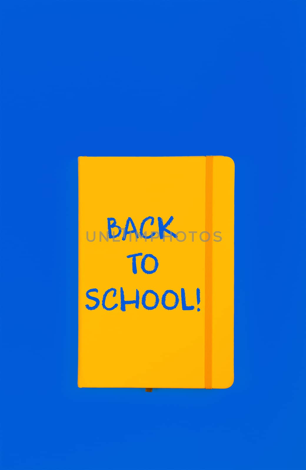 Back to school handwritten sign on yellow leather cover notebook over blue paper background with copy space