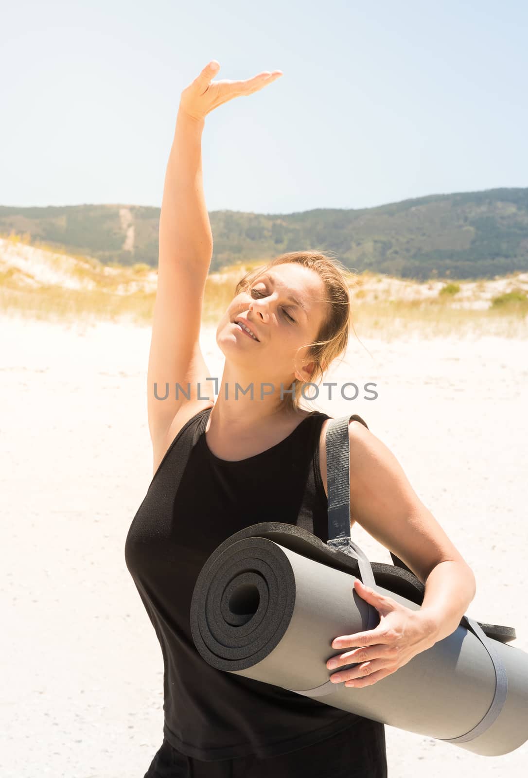 Woman in sportswear with a rolled-up mat under her arm at the beach by JRPazos