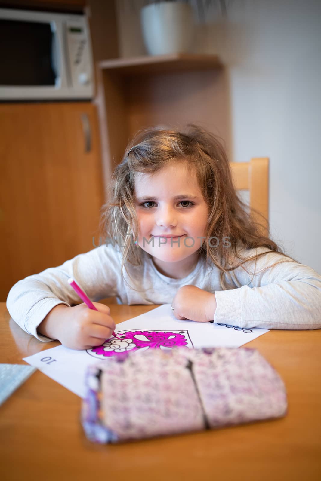 Smiling happy cute girl with long curly golden hair artist painting picture on paper. School homework concept