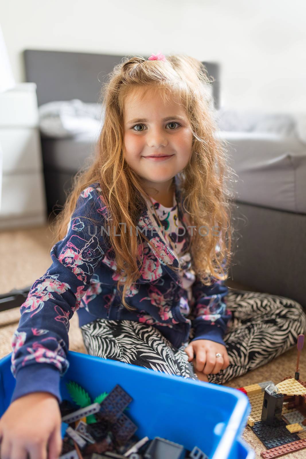 Smiling cute girl with long curly golden hair, charming preschooler cute child plays with child's building kit.