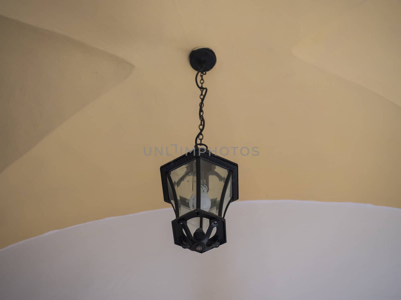 Electric black vintage lamp or lantern hanging on a chain under a vaulted yellow and white ceiling. Copy space.