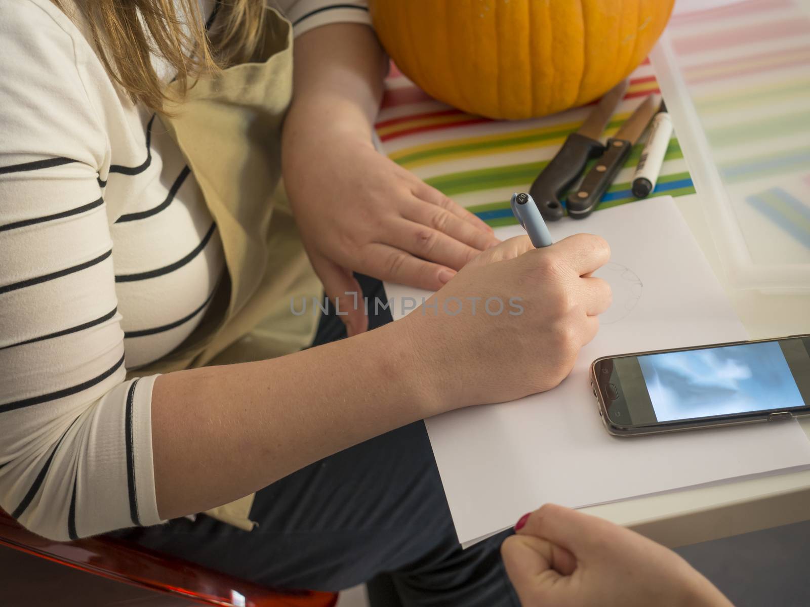 Process of carving pumpkin to make Jack-o-lantern. Creating traditional decoration for Halloween and Thanksgiving. Woman drawing decor on big orange pumpkin.