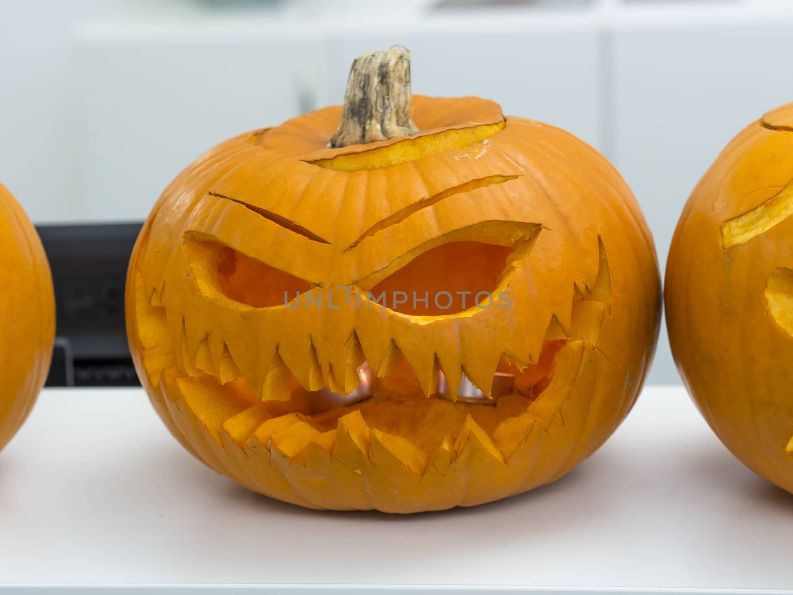 Halloween big orange pumpkin decorated with scary face. Jack O' Lantern on white table background.