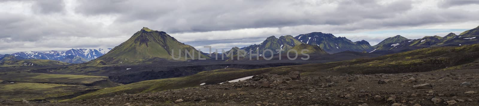 Colorful wide panorama, panoramic view on volcanic landscape in Nature reserve Fjallabak in central Iceland with green Maelifell hill and blue snow covered mountain range, moody sky background by Henkeova