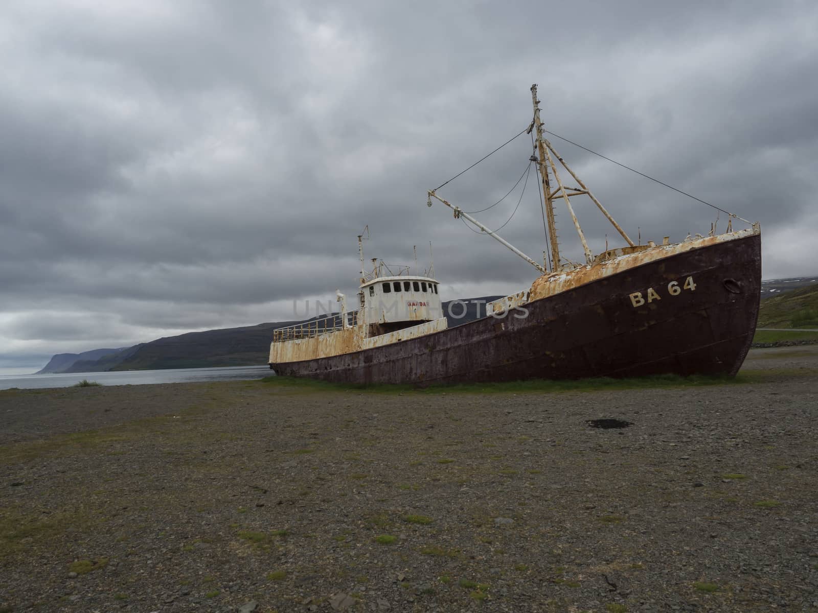 Iceland, west fjords, Patreksfjordur, June 24, 2018: Old abandoned rusty fishing boat ship wreck standing on the sand beach coast in west fjords od Iceland, dramatic gray sky and cliffs background by Henkeova