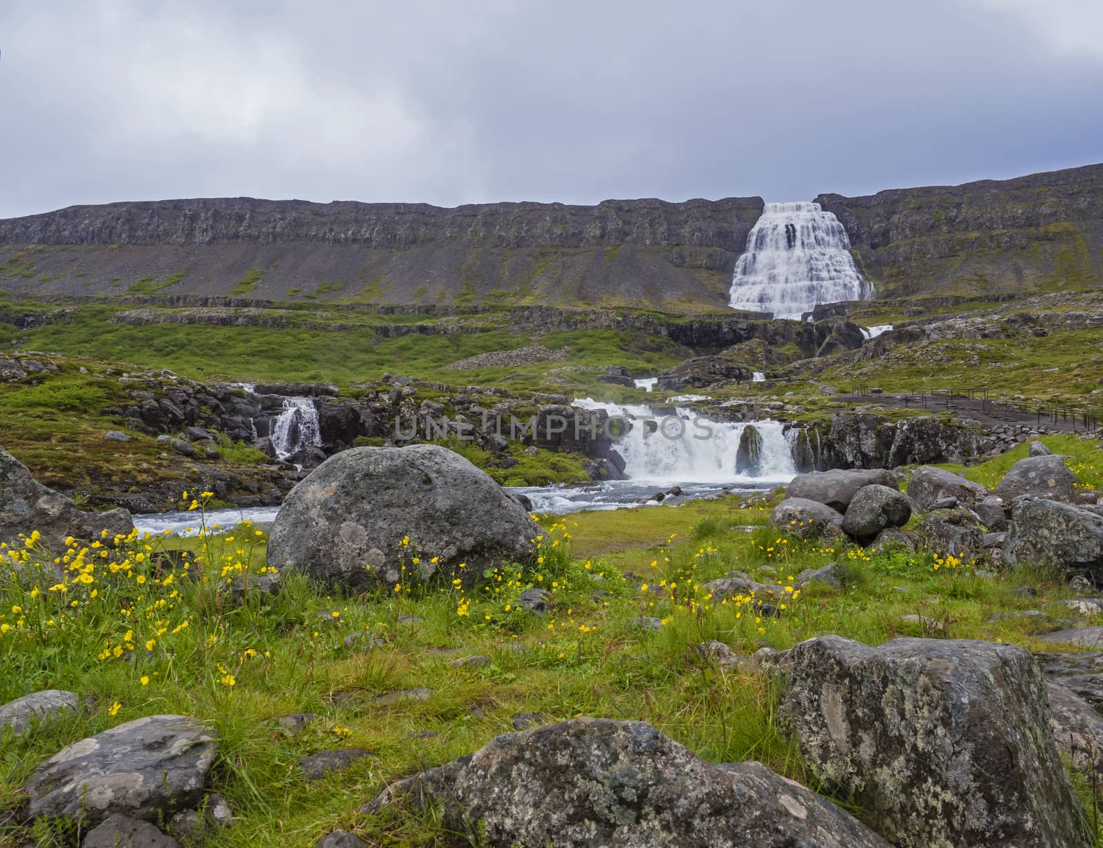 Dynjandi waterfall, biggest in west fjords of Iceland in summer, rock, mossed hills, river stream and blue sky background by Henkeova