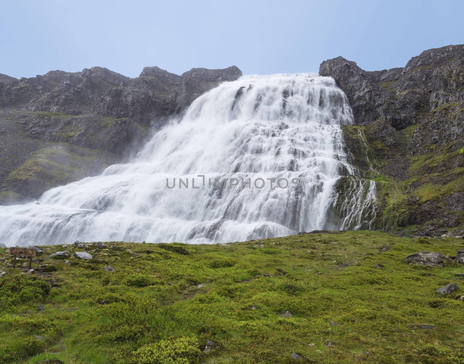 Dynjandi waterfall, biggest in west fjords of Iceland in summer, rock, green grass and blue sky background