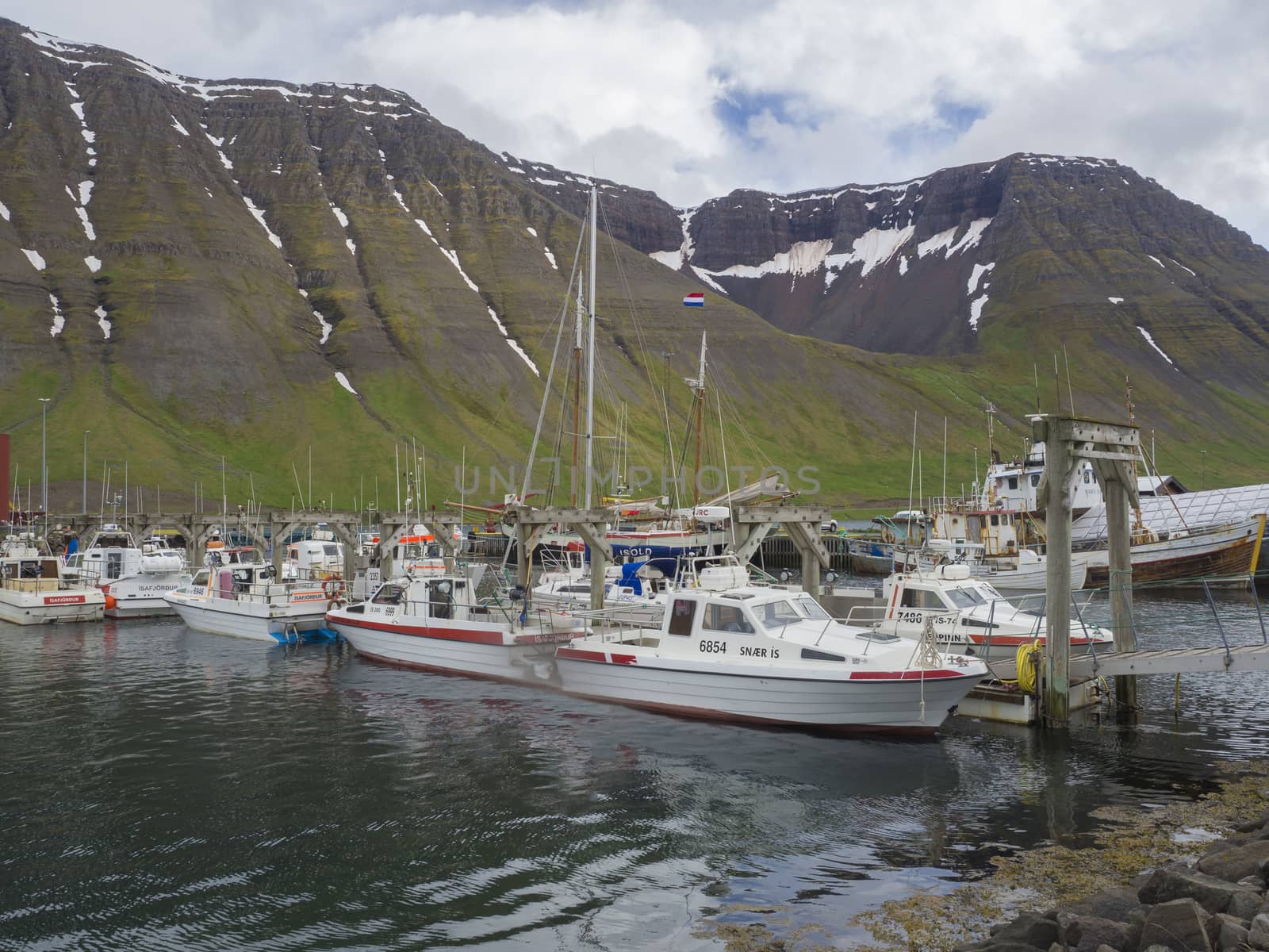 Iceland, West fjords, Isafjordur, June 25, 2018: summer view on Isafjordur harbor with fishing boats ships and beautiful green snow covered mountains and cliffs, clouds and blue sky background