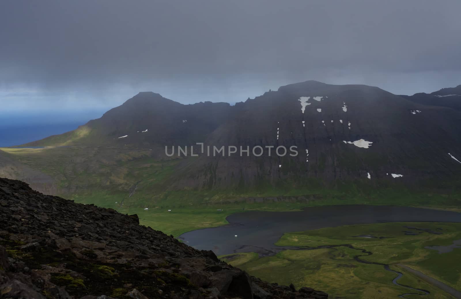 Northern summer landscape, View on beautiful snow covered cliffs and fljotsvatn lake in Fljotavik cove in Hornstrandir, west fjords, Iceland, with river stream, green grass meadow, moody sky by Henkeova