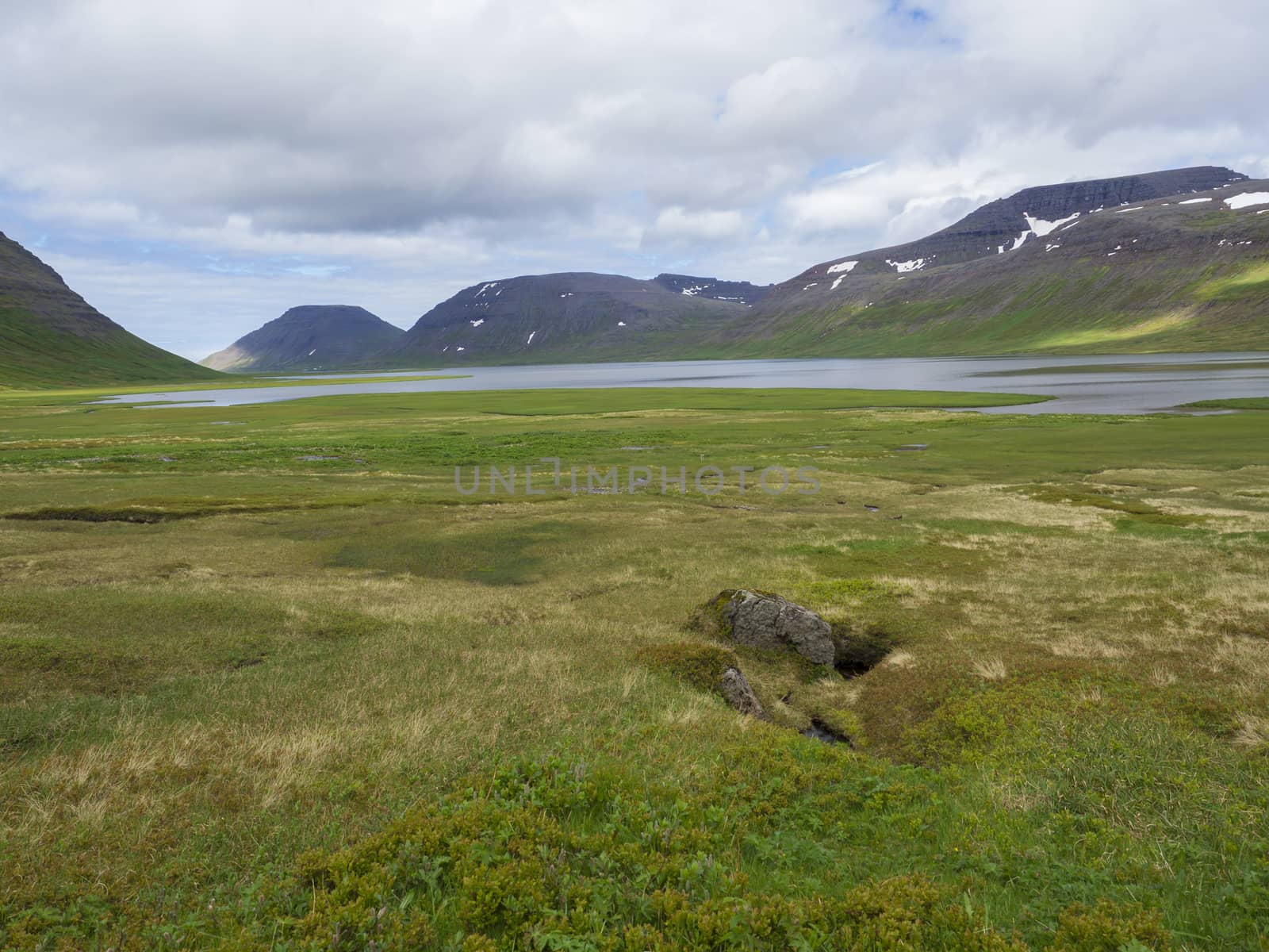 Northern summer landscape, beautiful snow covered cliffs and fljotsvatn lake in Fljotavik cove in Hornstrandir, white clouds sky background