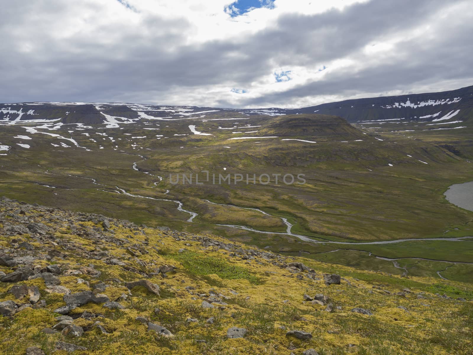 View on adalvik and latrar in west fjords nature reserve Hornstrandir in Iceland with lake and river stream, green grass meadow, beach, ocean, hills and dramatic cliffs, dark cloudy sky background