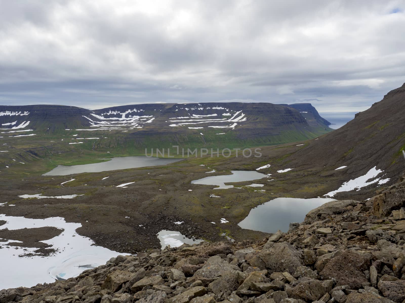 Northern summer landscape, beautiful snow covered cliffs and fljotsvatn lake in Fljotavik cove, rocks and grass meadow, moody sky background, Hornstrandir, west fjords, Iceland by Henkeova