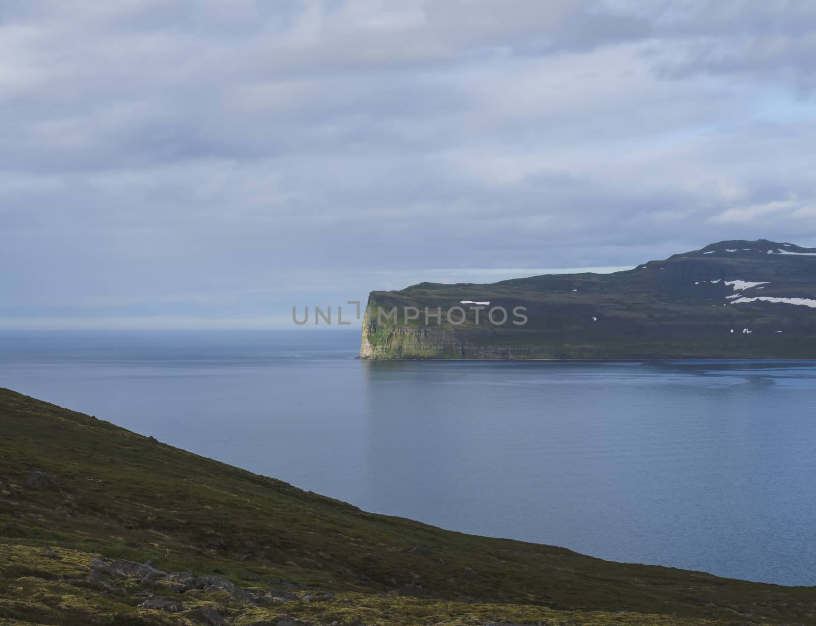 Scenic view from ocean on beautiful snow patched cliffs in west fjords, nature reserve Hornstrandir in Iceland, blue sea and cloudy sky background, golden hour light by Henkeova