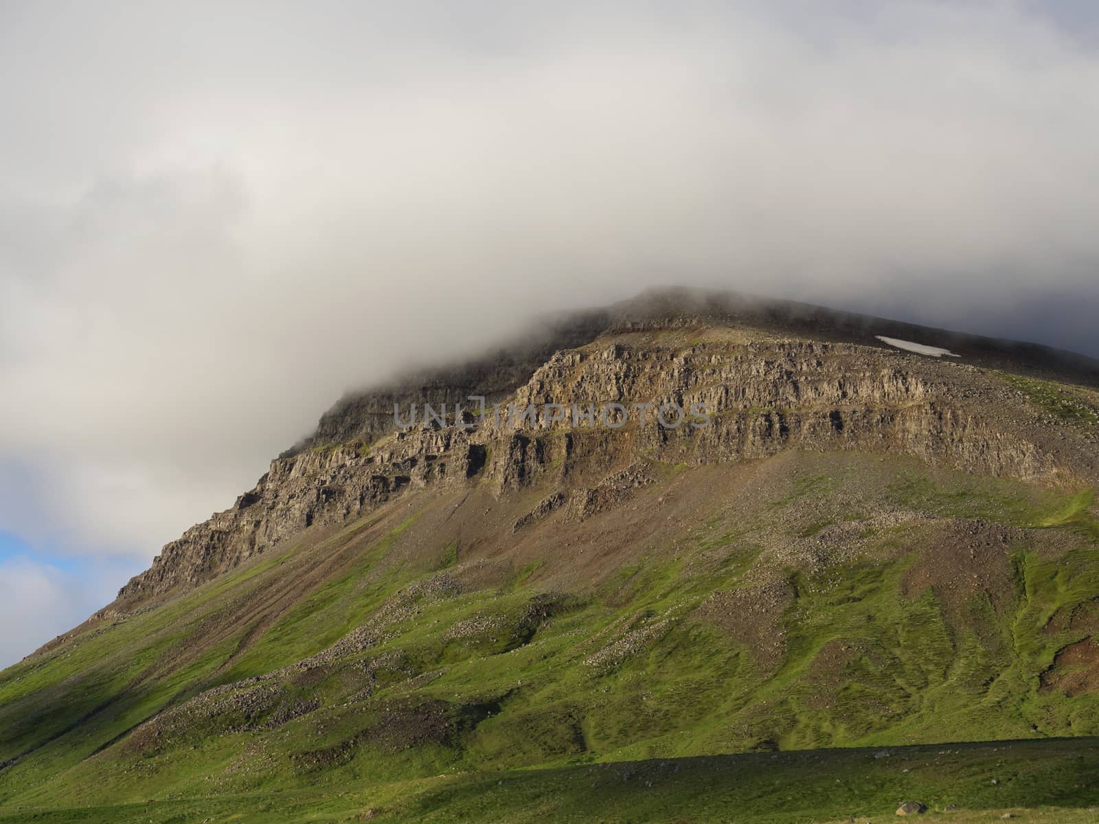 Landscape with green mountain peak covered in fog, golden light west fjords Iceland, copy space