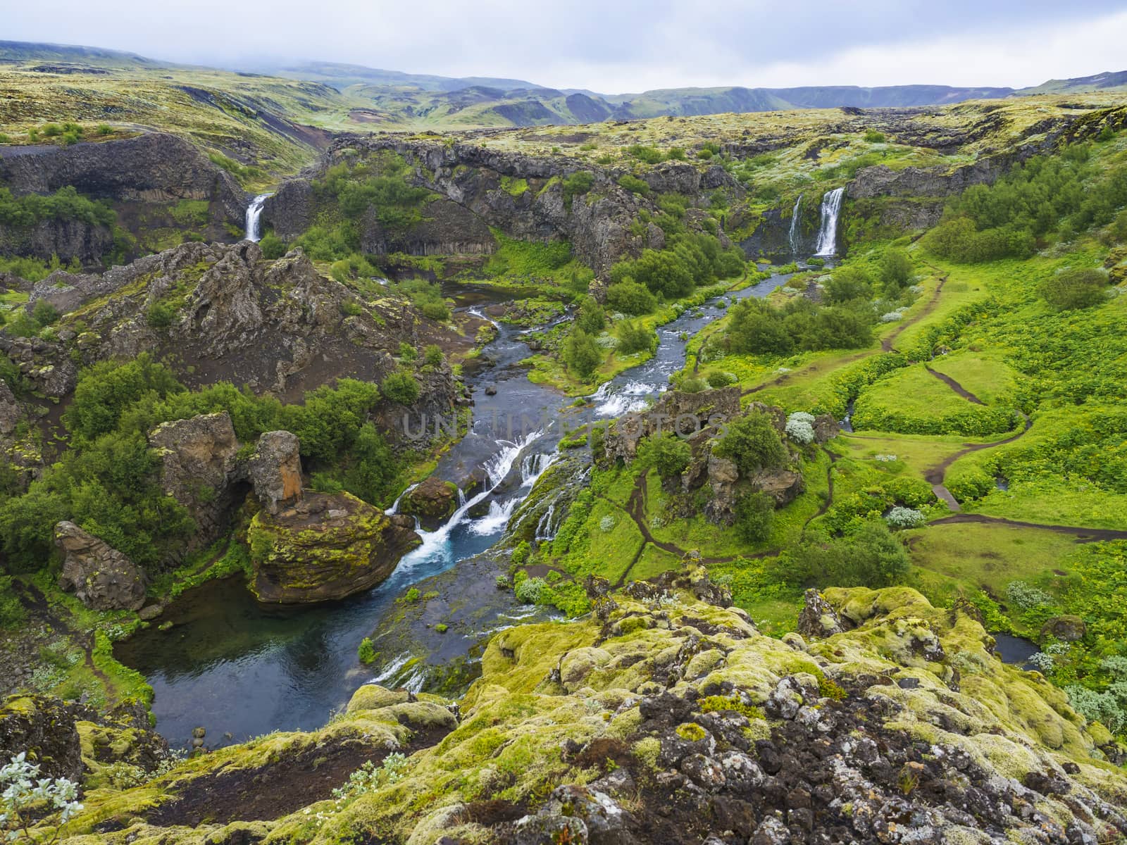 Beautiful Valley Gjain with colorful lava rocks, lush green moss and vegetation and blue water with waterfalls and cascade in south Iceland.