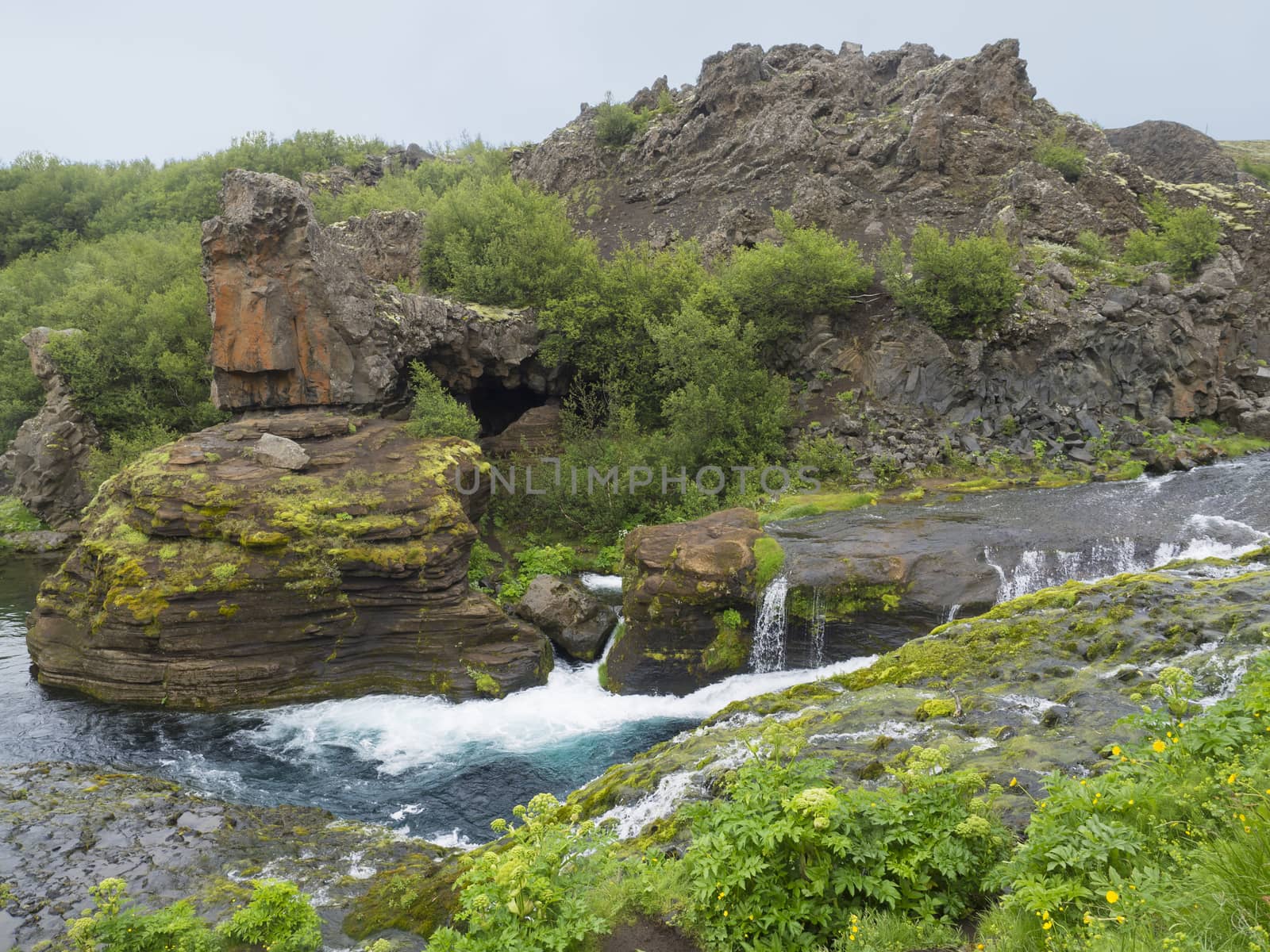 Beautiful Valley Gjain with colorful lava rocks, green vegetation and blue water stream cascade in south Iceland