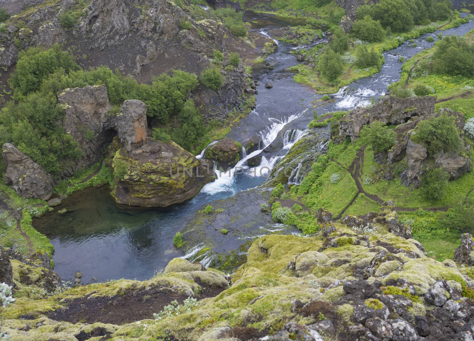 Beautiful Valley Gjain with colorful lava rocks, green vegetation and blue water stream cascade in south Iceland