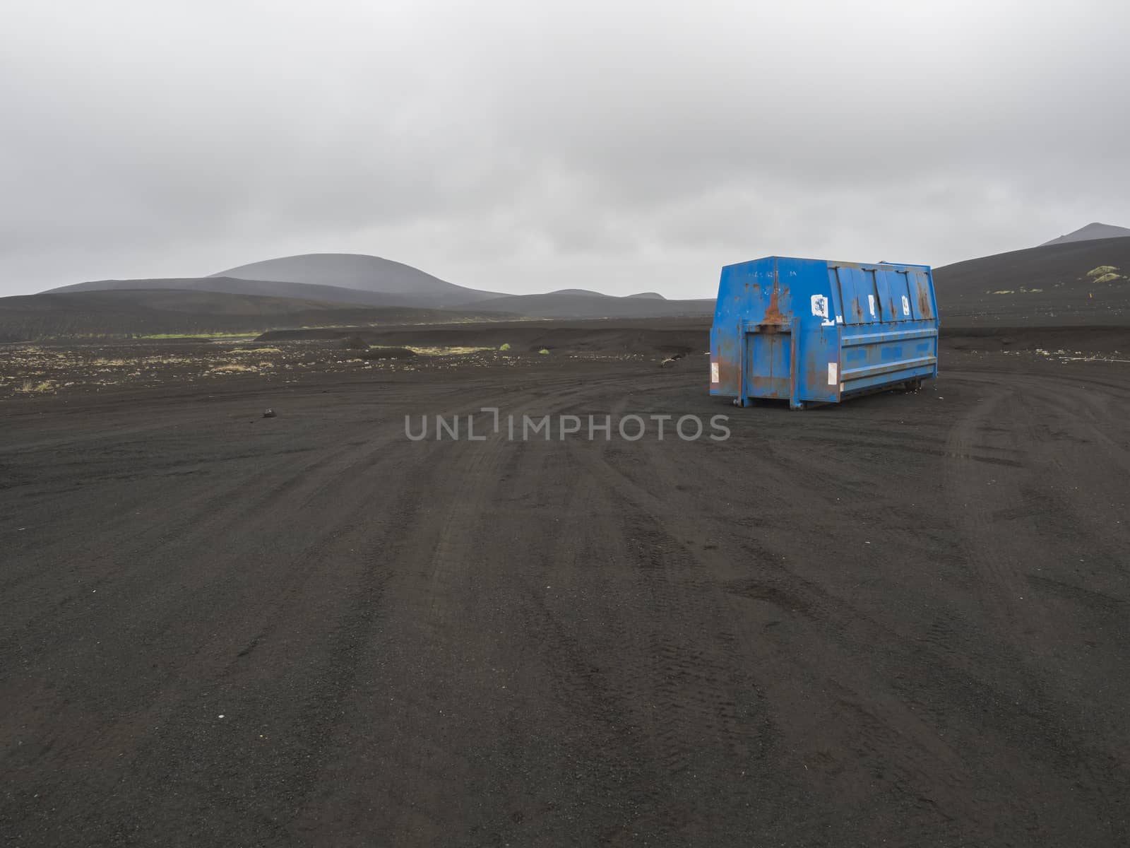 blue metal garbage container standing alone in black lava sand desert in Iceland, hills and gray sky background, copy space