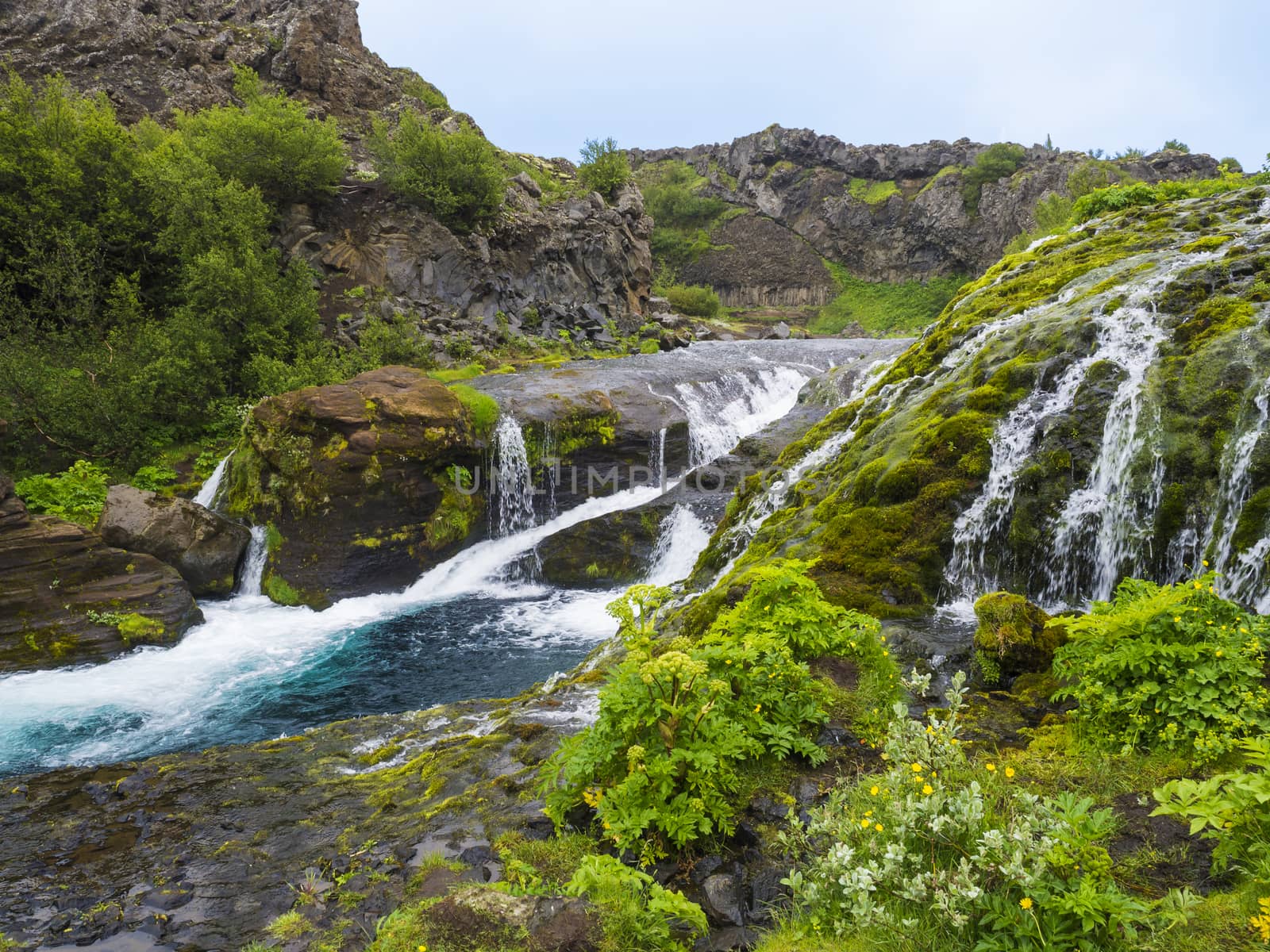 Beautiful Valley Gjain with colorful lava rocks, lush green moss and vegetation and blue water with waterfalls and cascade in south Iceland.