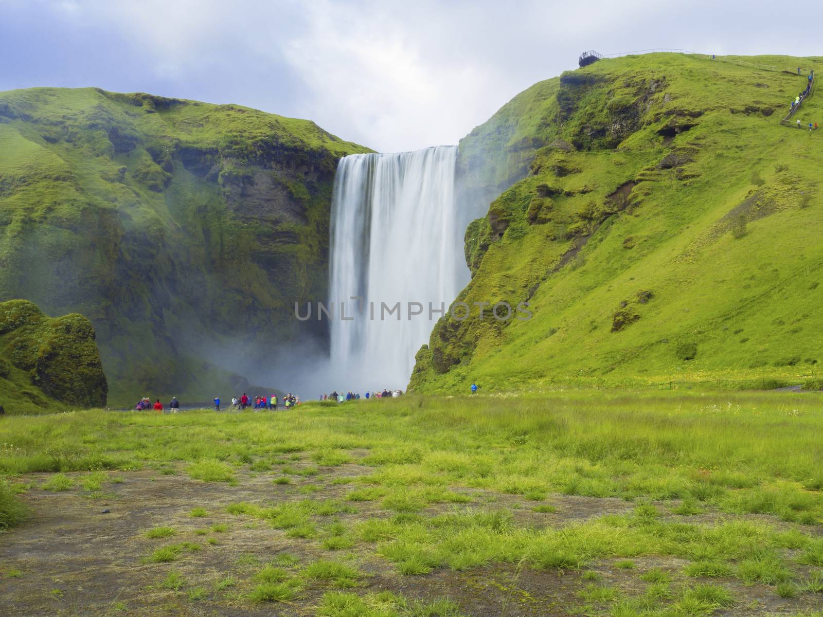 Beautiful Skogafoss waterfall in South Iceland Skogar with group of colorful dressed tourist people, long exposure motion blur, copy space