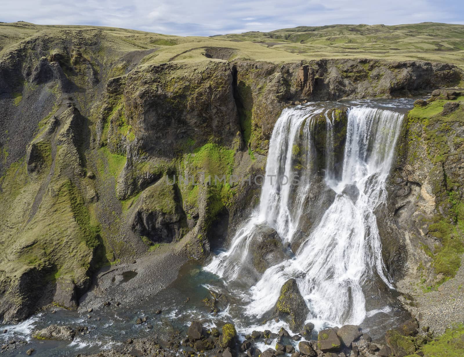 View on Beautiful Fragifoss waterfall on Geirlandsa river in South Iceland, green moss and rock, blue sky background