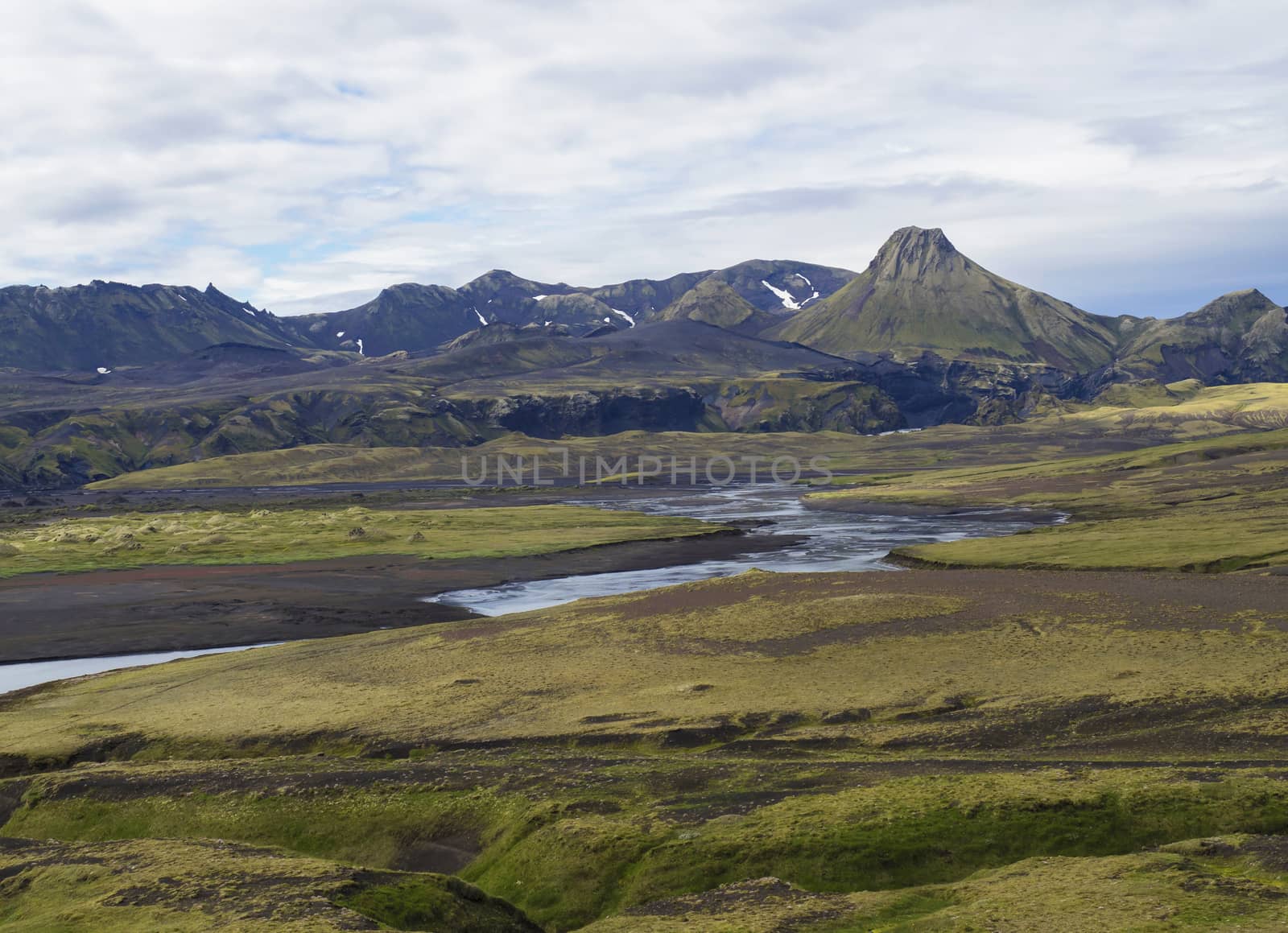 mountain range on road F210 in abandoned green landscape at Nature reserve Fjallabaki in Iceland with colorful snow and moss capped rhyolite mountains, wild river stream, blue sky white clouds