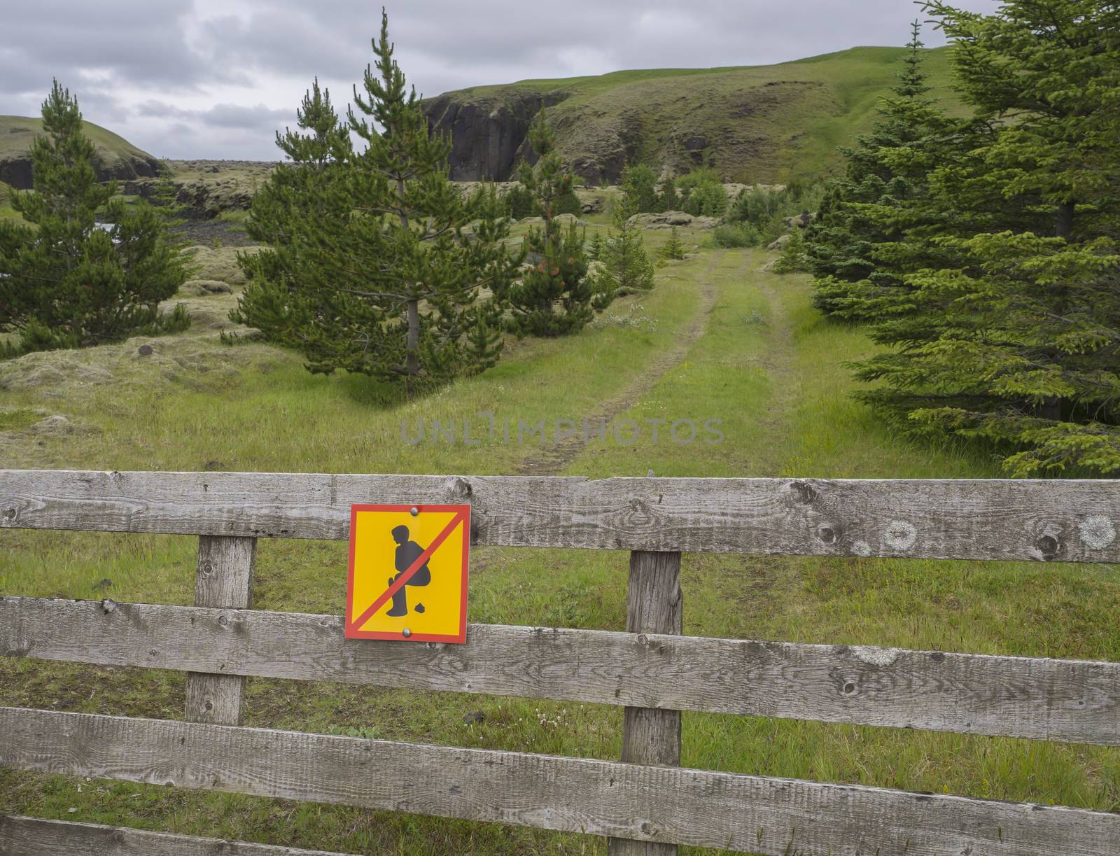 Warning sign Do not poop here for human, tourist people, on wooden fence, beautiful green iceland landscape in background