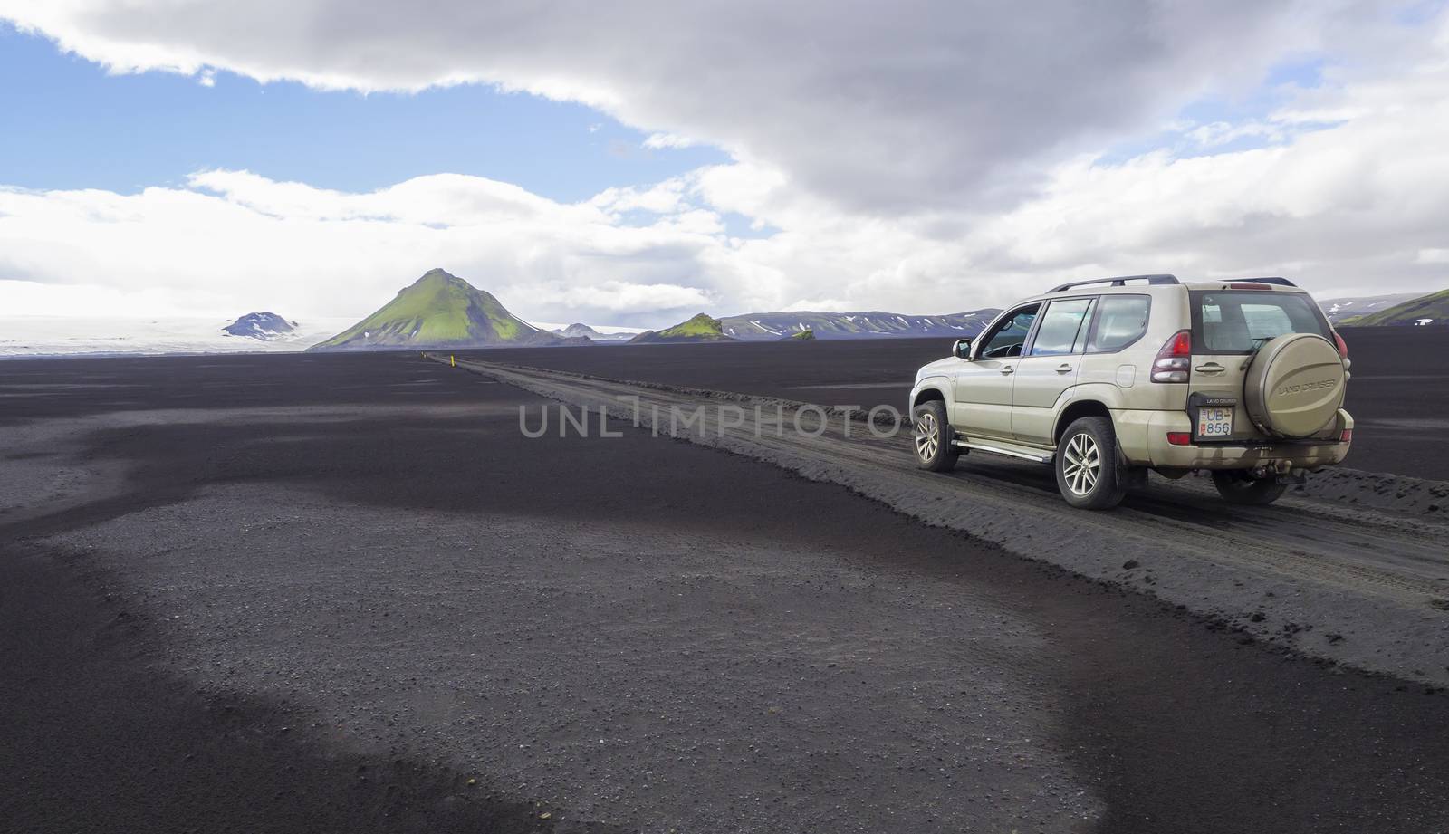 South Iceland, Nature reserve Fjallabak, July 7, 2018: Off road car Toyota Landcruiser driving on dirt mountain road F210 through black lava sand desert with green Maelifell mountain and myrdalsjokull glacier, blue sky white clouds