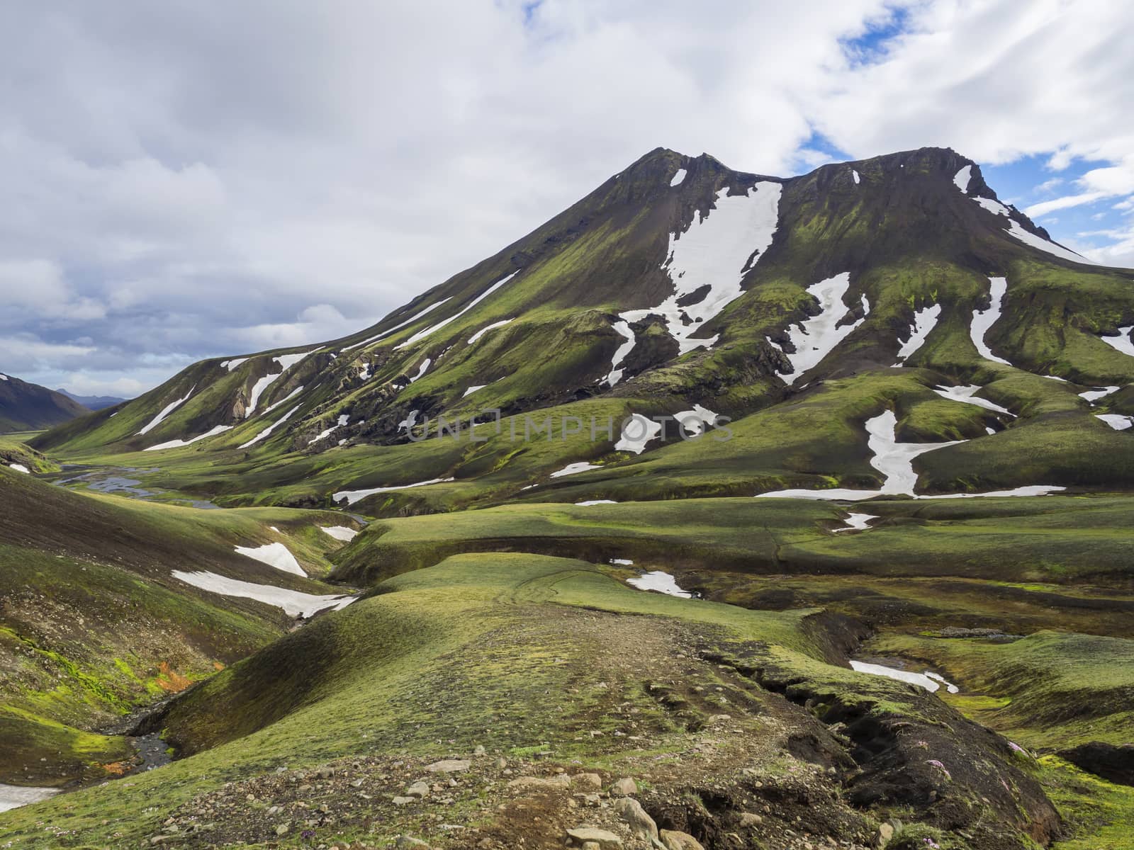 View on green moss and snow covered vulcanic mountain and creek stream in Maelifellssandi near road f210 in Iceland natue reserve Fjallabaki, white clouds blue sky