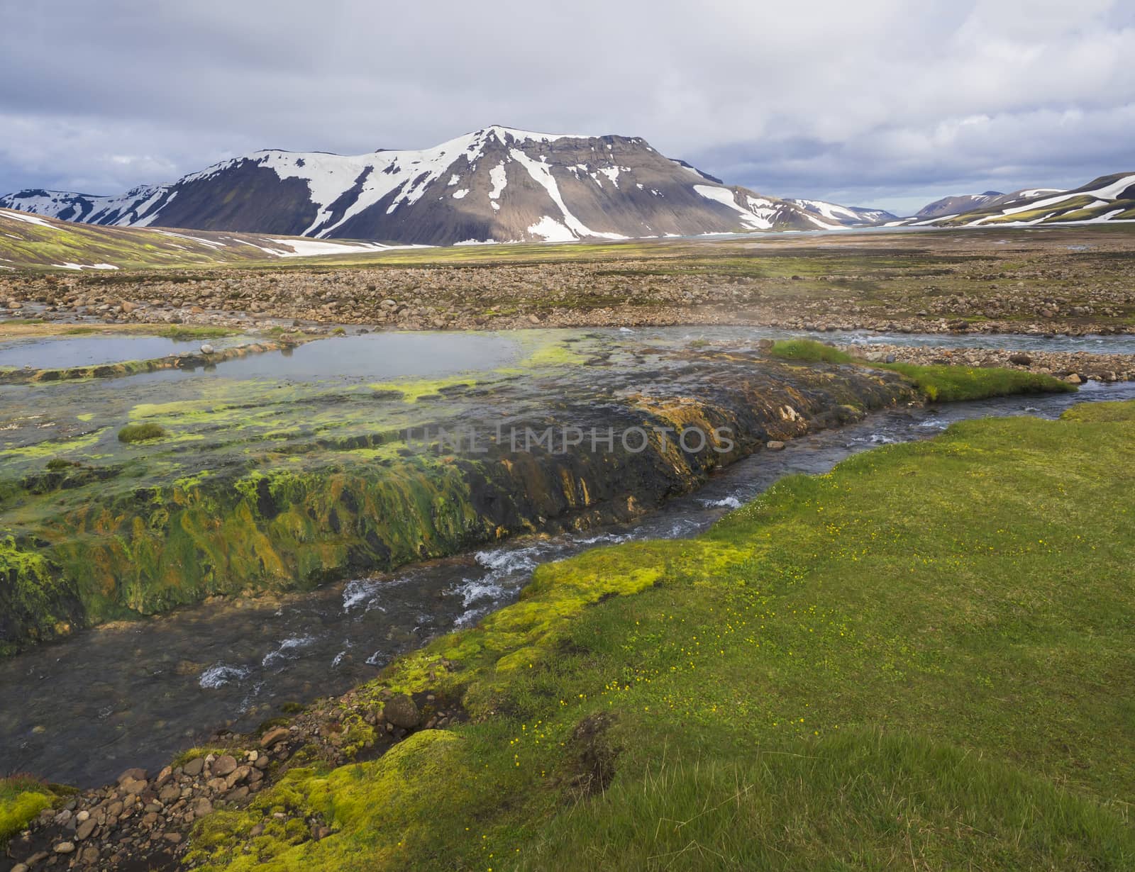 summer landscape with colorful green and orange moss meadow with hot pool Strutslaug and spring with snow capped rhyolite mountains in geothermal area near road f210 in Iceland nature reserve Fjallabaki