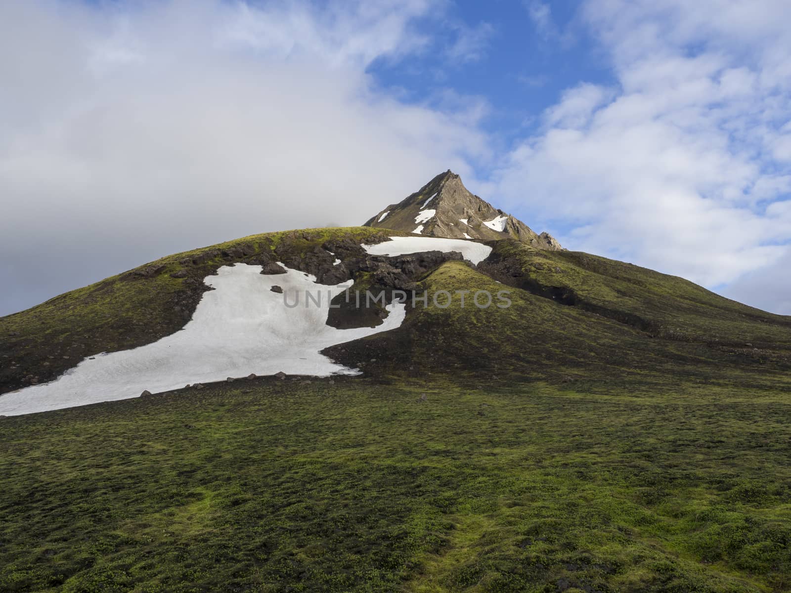 Landscape with snow capped mountain peak, pyramide shape in central highlands Iceland, blue sky white clouds, golden light