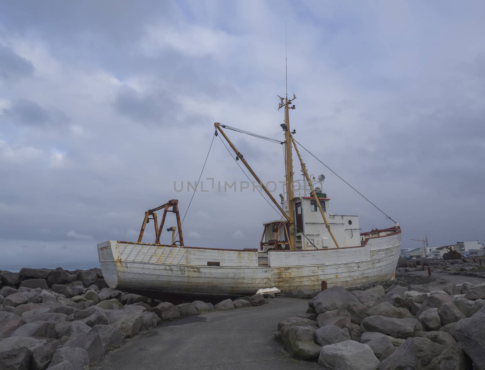 old rusty abandoned fishing boat, ship wreck standing on rock, sea bank promenade in Keflavik, Iceland, blue sky clouds background