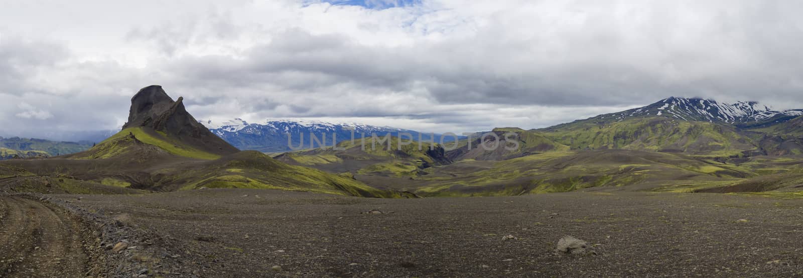 Colorful wide panorama, panoramic view on volcanic landscape in Nature reserve Fjallabak in central Iceland with mountain einhyrningur with green moss and blue snow covered mountain range, moody sky