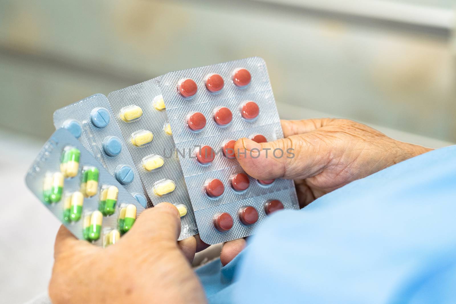 Asian senior or elderly old lady woman patient holding antibiotics capsule pills in blister packaging for treatment infection patient in hospital : Pharmacy drugstore concept. by pamai