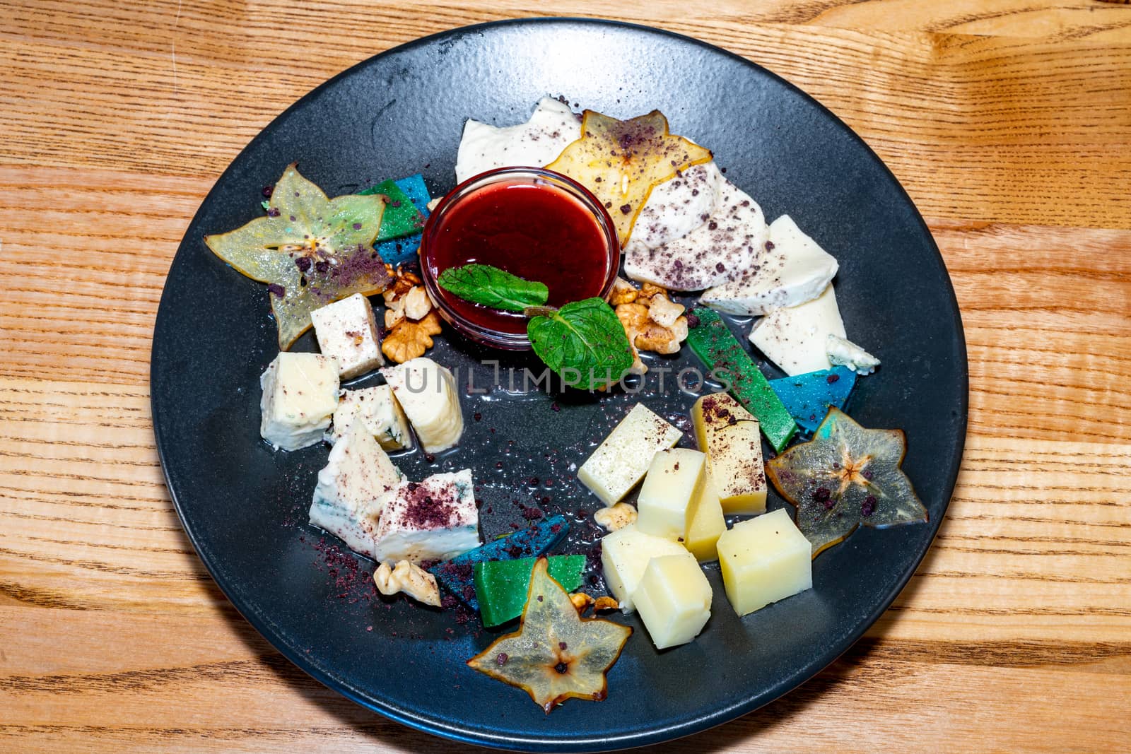 Farm cheeses. Three types of cheese and sauce on a black plate