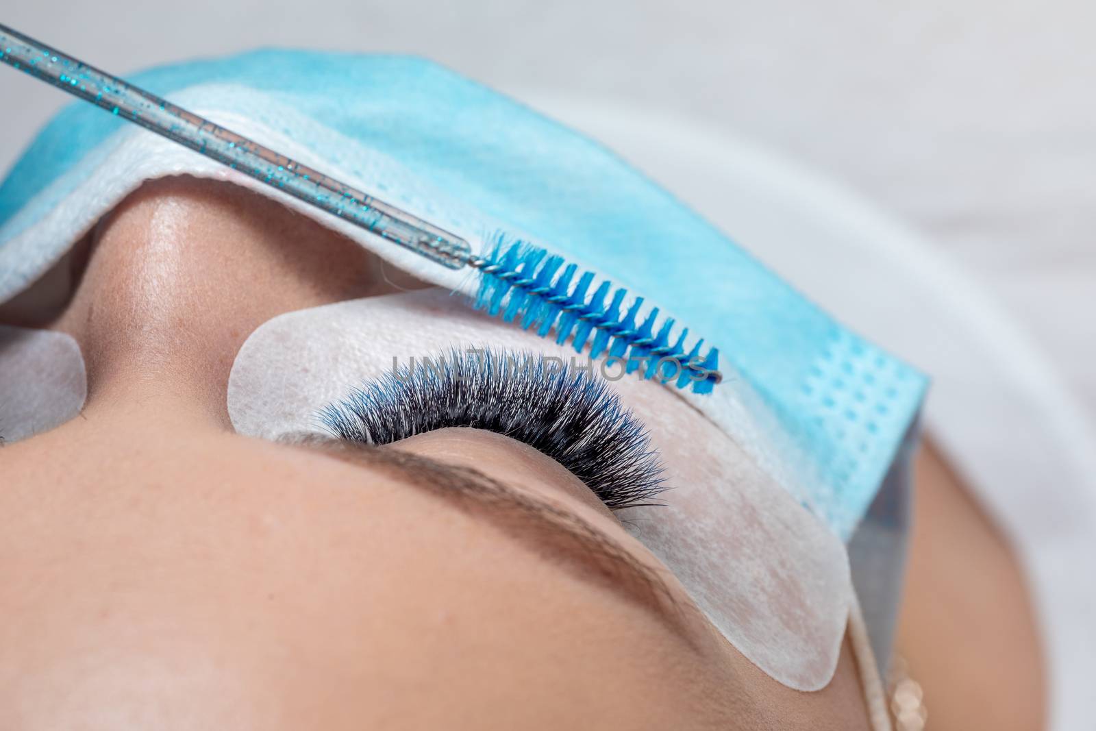 Treatment of Eyelash Extension in blue color Lashes. Eyes with Long Eyelashes and face with facemask