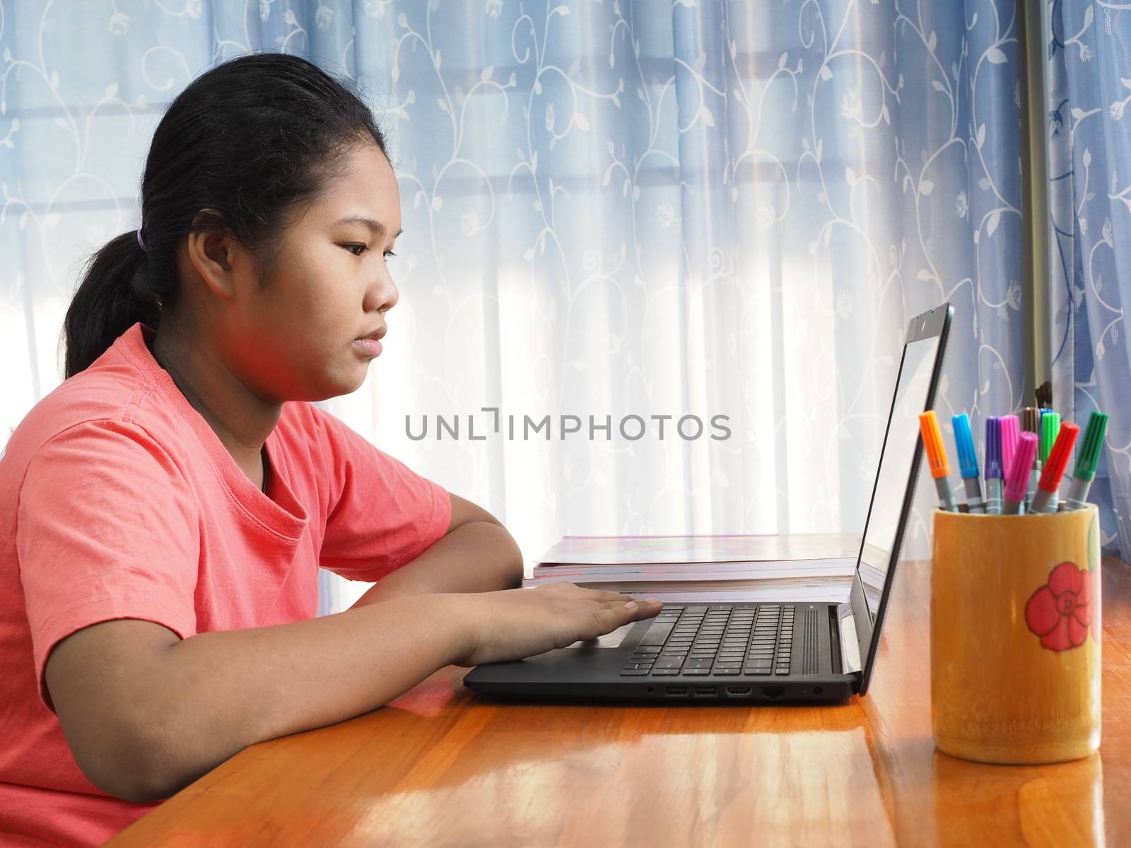 An Asian girl is watching a computer screen to learn online on a by Unimages2527