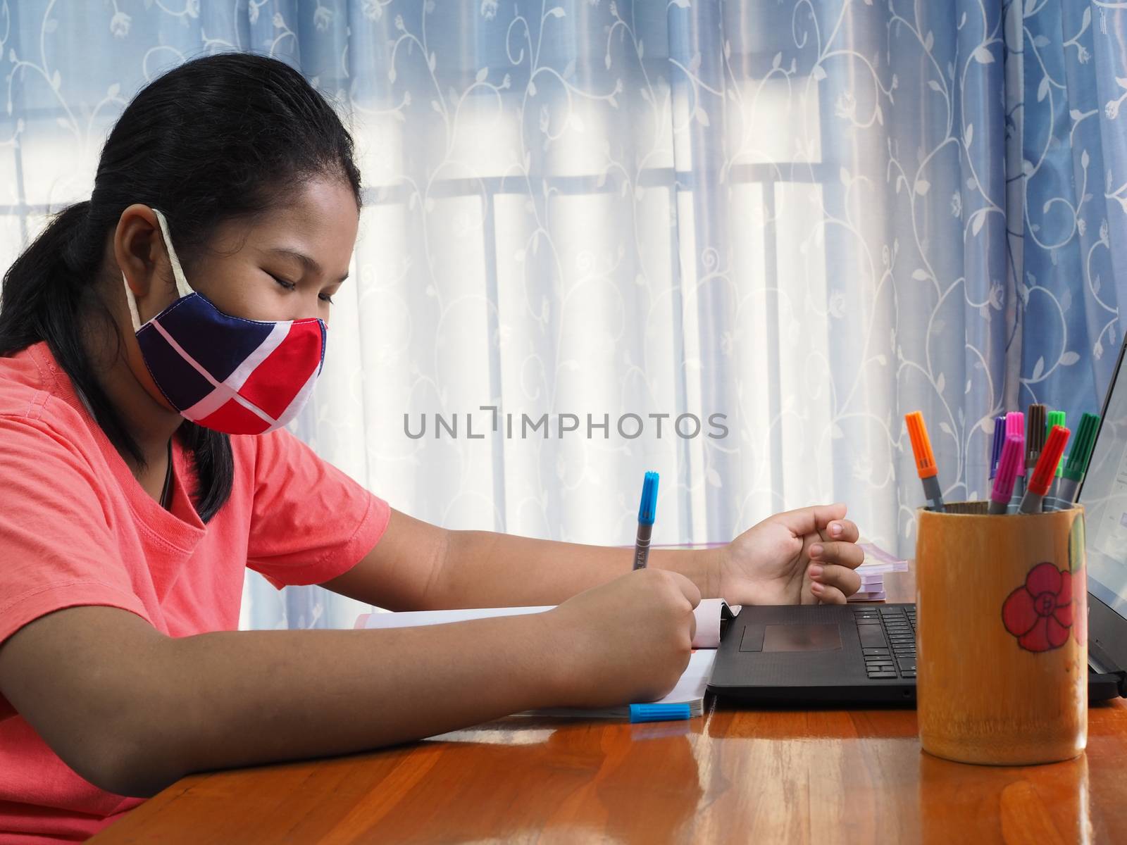 An Asian girl wearing a cloth mask and Sitting and studying at home In his own room. At the time of the corona virus outbreak.
Learning from home concepts.
Concept of e-learning.
new normal concept.