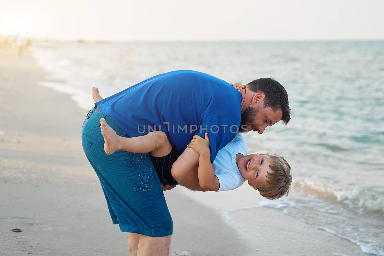 Father son spending time together sea vacation Young dad child little boy walking beach Fathers day. Family with one child. Happy childhood with daddy. sitting on hands laughs