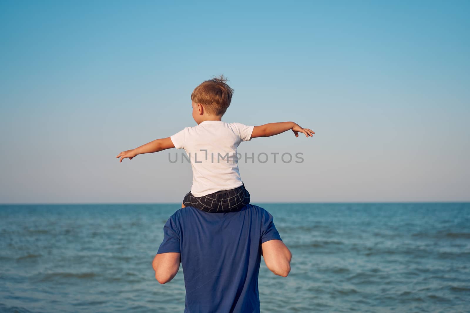 Father son together outside showing finger sea horizon Man child spending time vacation enjoying summer Family with one child. Caucasian person beach Little boy sit on man shoulders Flying with hands