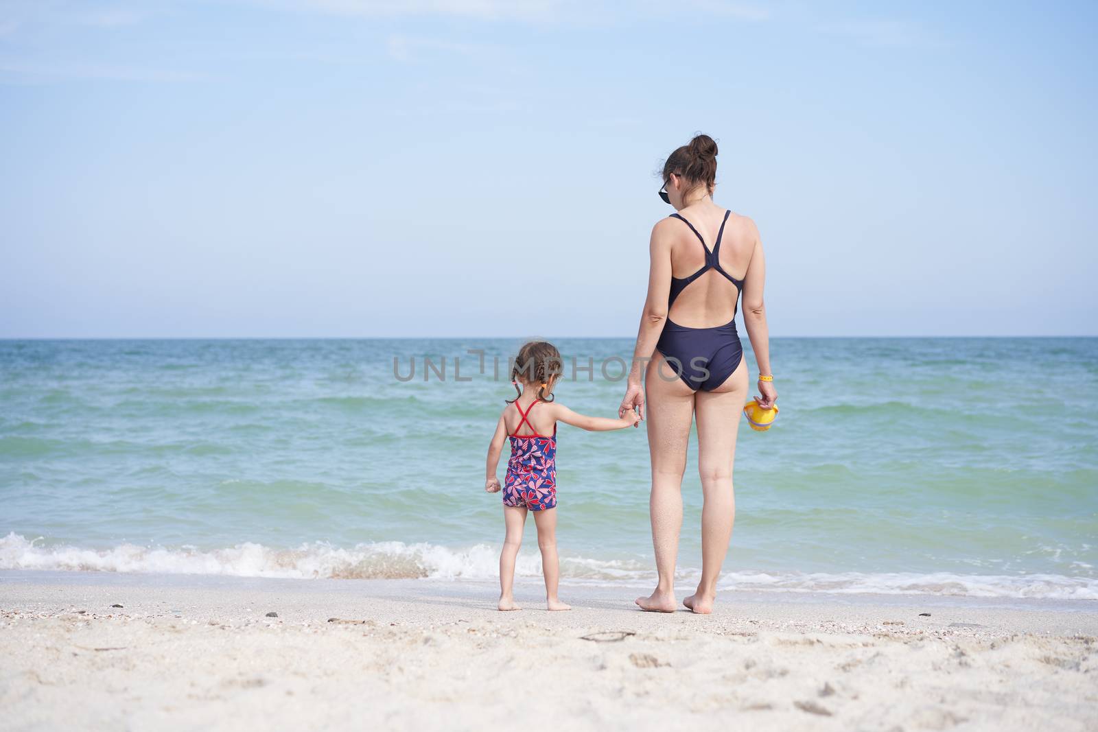 Mother daughter beach together rear view Unrecognizable caucasian woman little girl swimwear standing seaside back Family with one child. Family Vacation Summertime