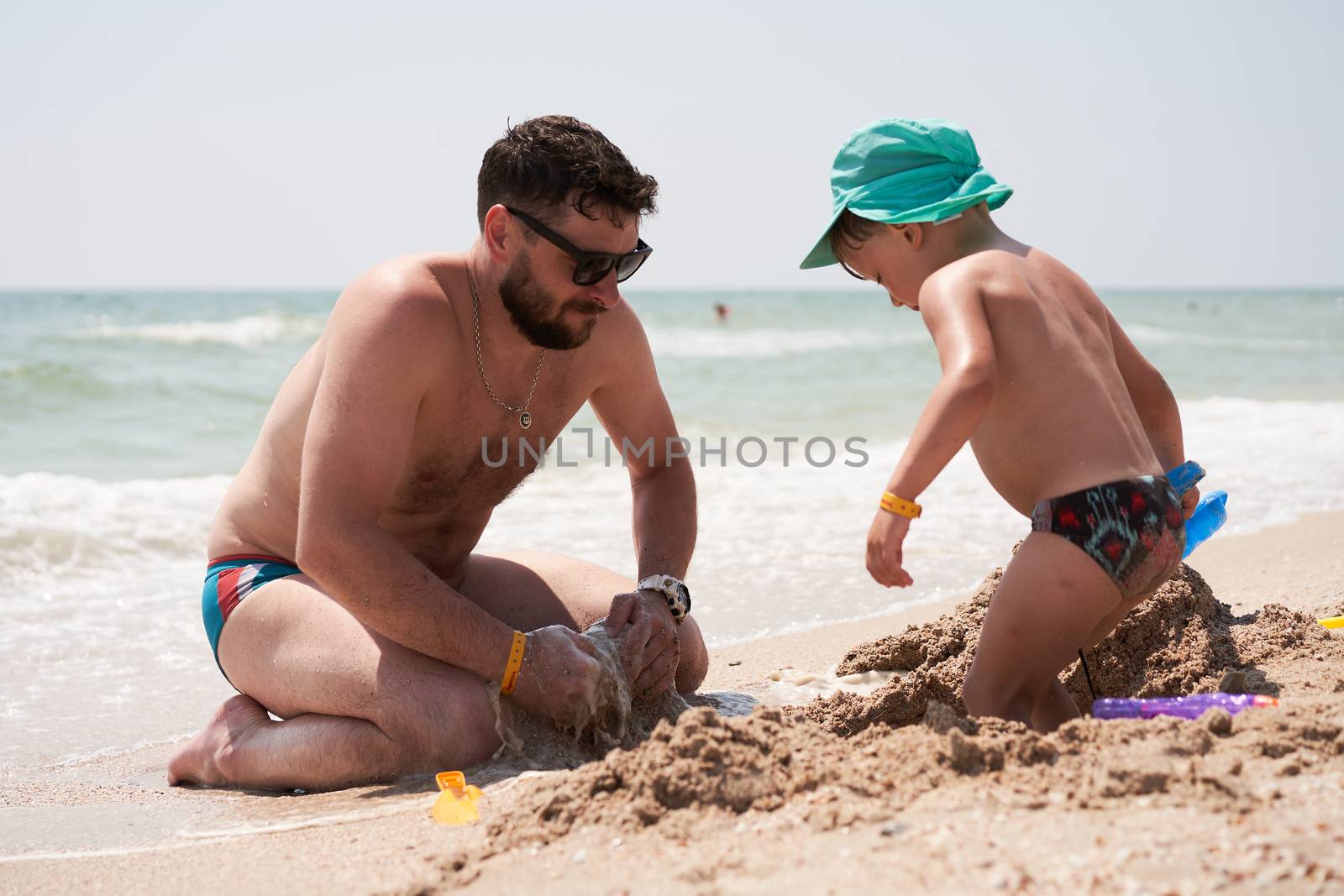 Father son together summer vacation playing sand sea beach Dad kid enjoyment togetherness weekend activity. by andreonegin