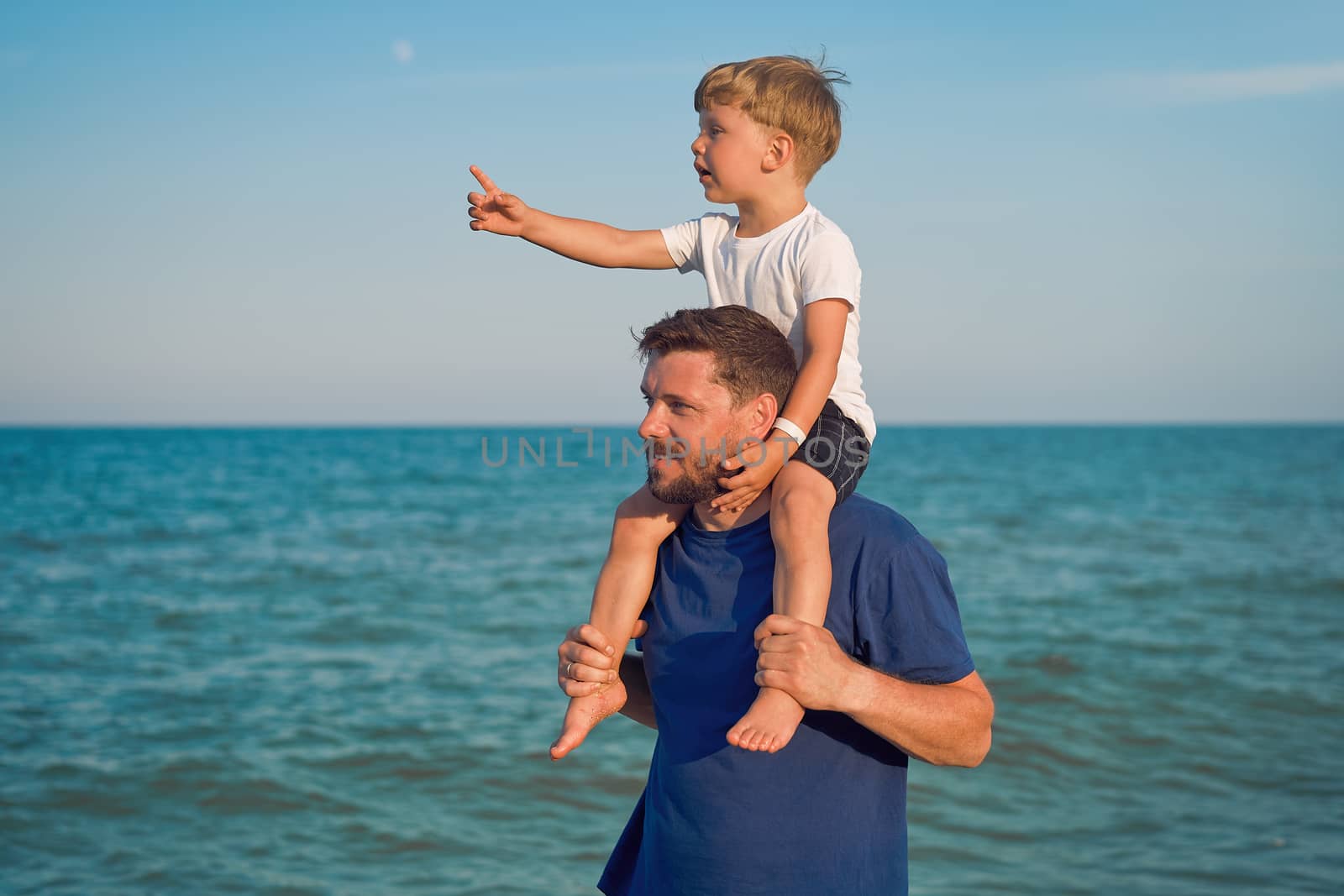 Father son together outside showing finger sea horizon Man child spending time vacation enjoying summer Family with one child. Caucasian person beach Little boy sit on man shoulders