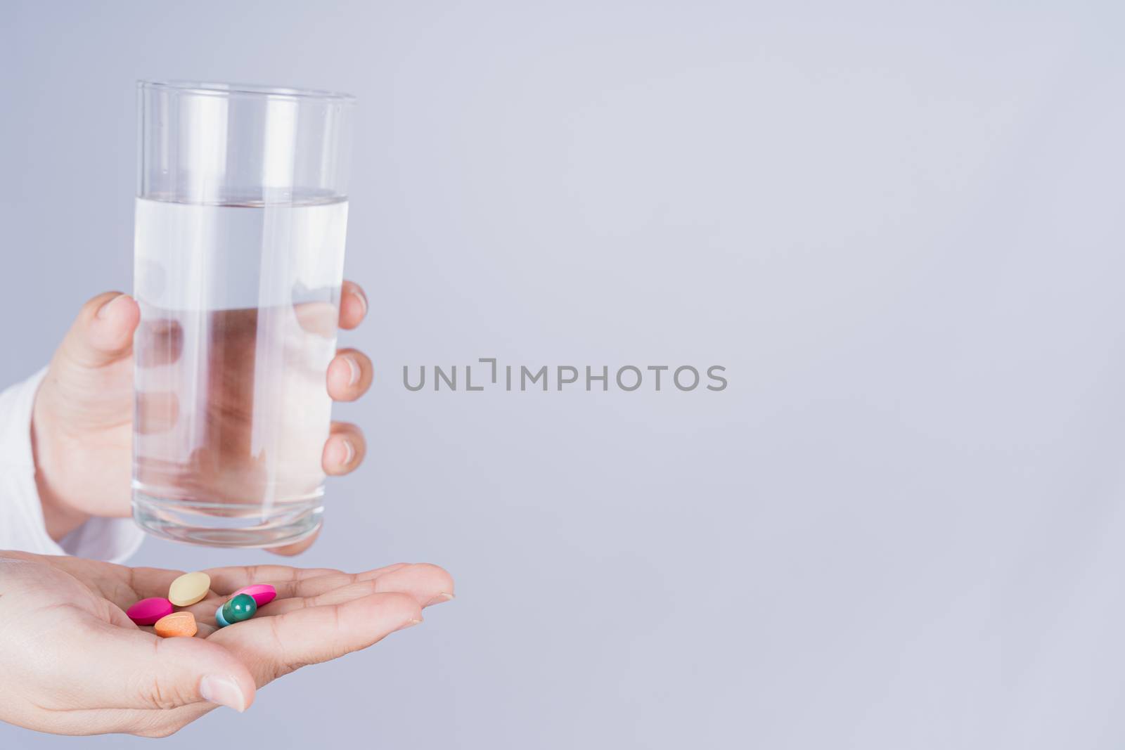 Close up Asian woman holding a glass of water and pill drugs in hand on grey background. Healthcare and medical pharmacy concept