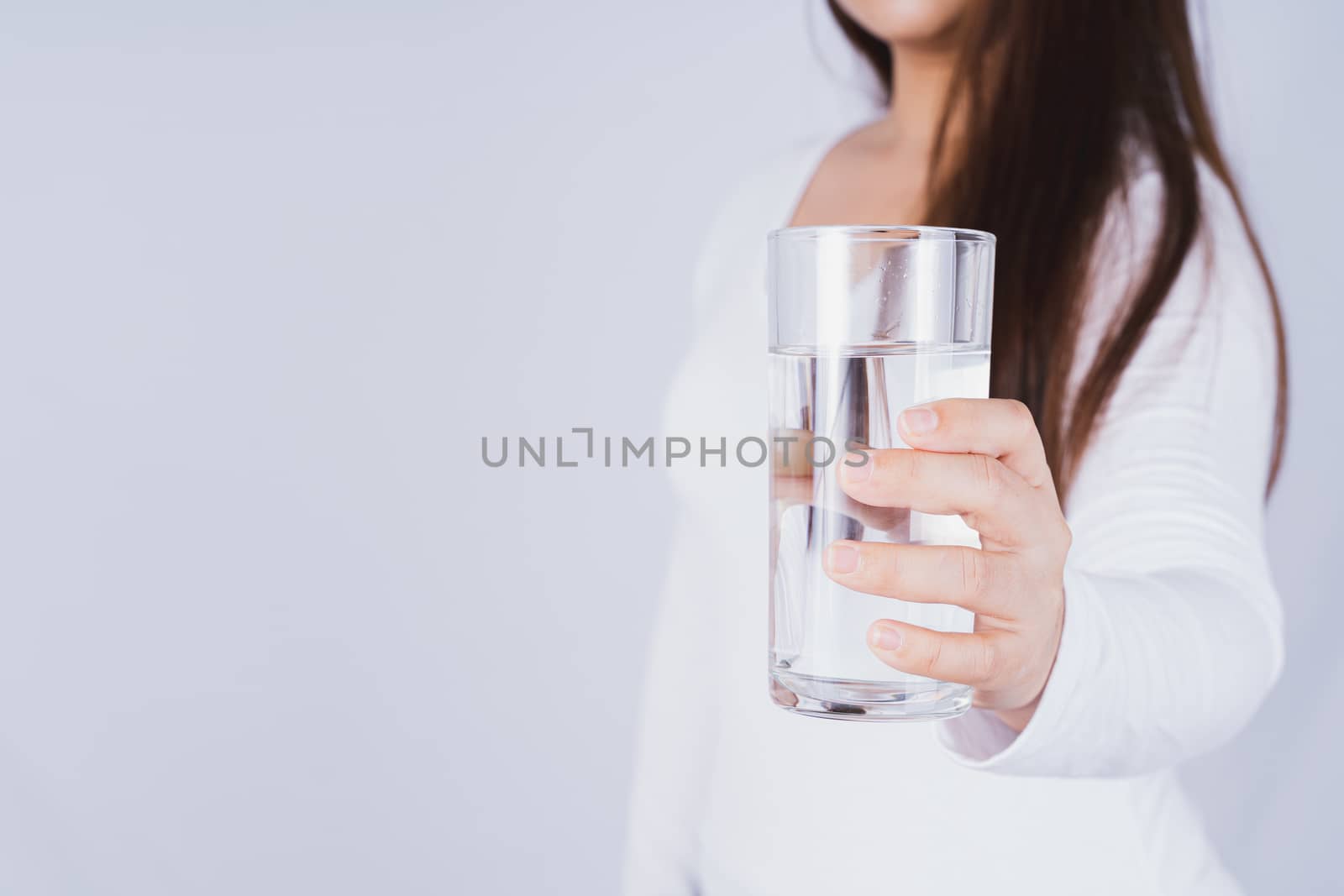 Close up Asian woman holding a glass of water in hand on grey background. Healthcare and medical pharmacy concept