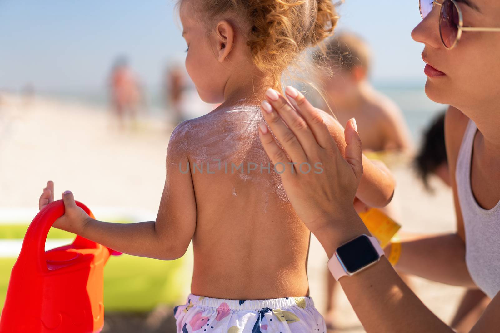 Caring mother apply sunblock to the back of her little daughter. Summer vacation sea beach by andreonegin